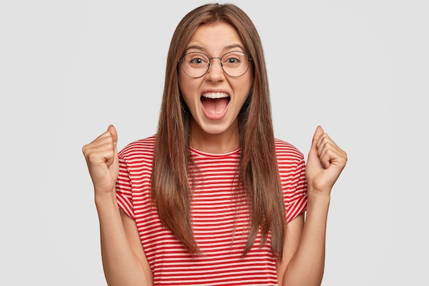 Free photo self determined woman with dark straight hair, clenches fists and exclaims with triumph expression