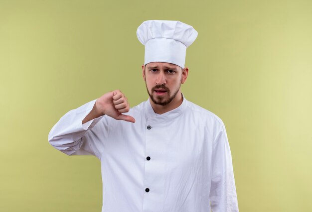 Self-satisfied professional male chef cook in white uniform and cook hat pointing to himself standing over gree background