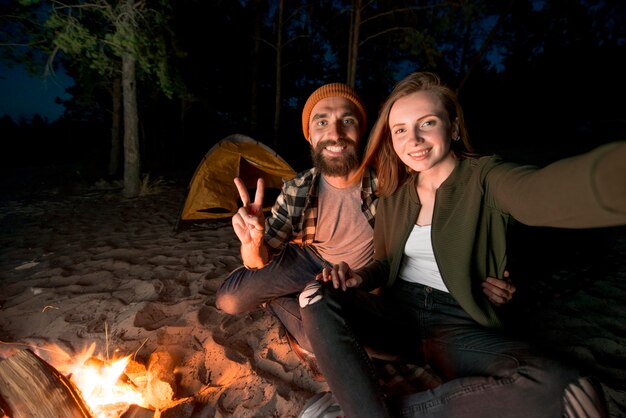 Selfie of couple camping at night by campfire