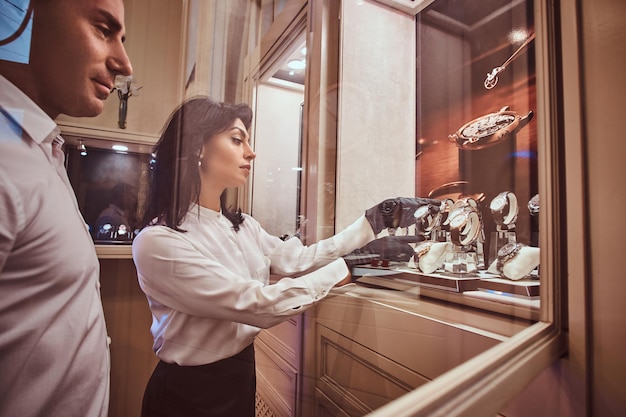 Free Photo seller shows the client an exclusive men's watch standing next to open showcase in the luxury jewelry store