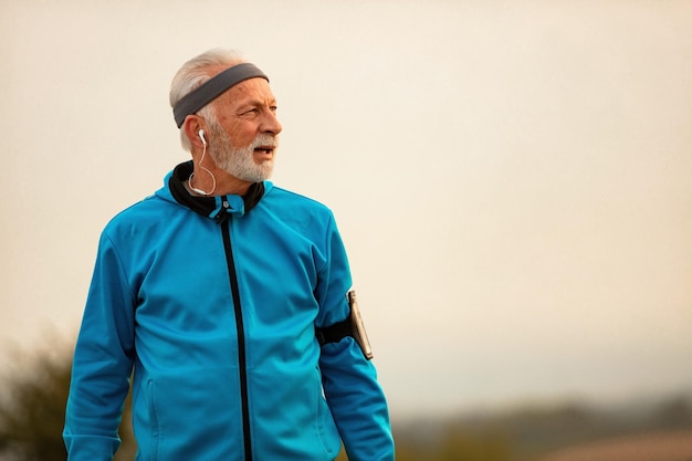 Free photo senior athlete determined to keep healthy lifestyle listening music on earphones while taking a break form exercising in nature copy space