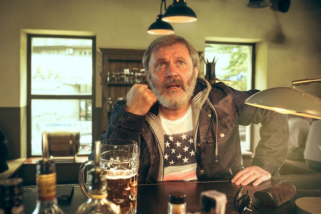 senior bearded man drinking beer in pub