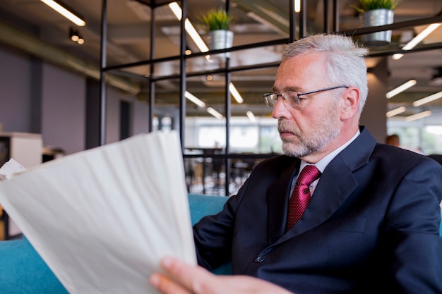 Free photo senior businessman sitting reading newspaper in the office