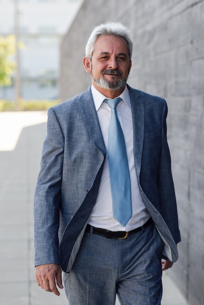 Senior businessman walking outside of modern office building.