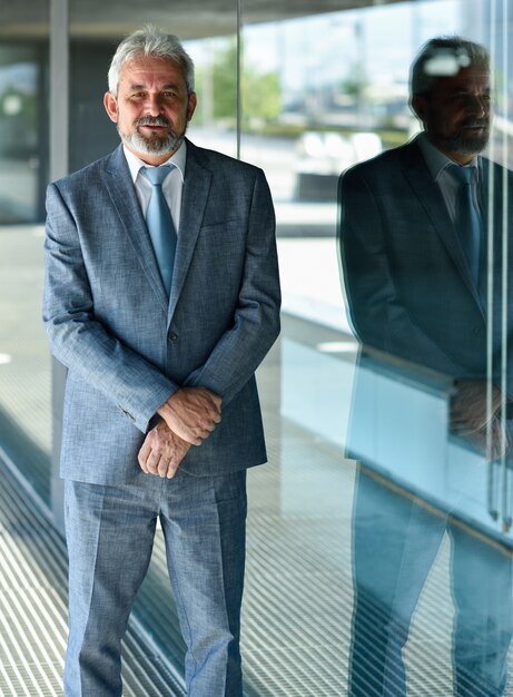 Senior businessman with arms crossed outside of modern office building.