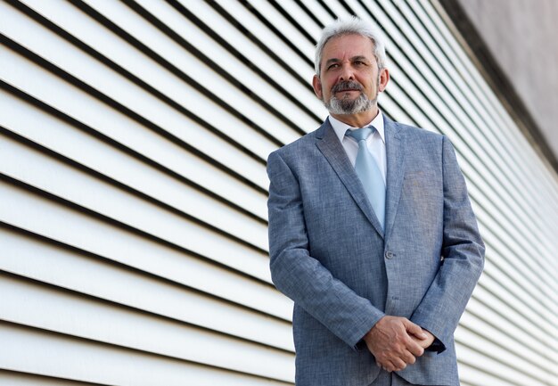 Senior businessman with arms crossed outside of modern office building.