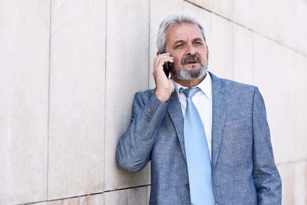 Senior businessman with smartphone outside of modern office building.