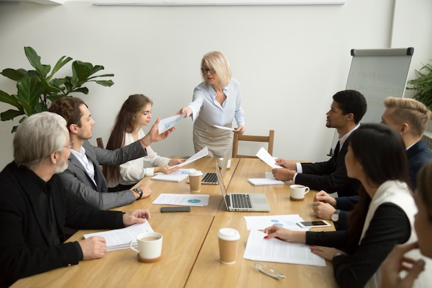 Senior businesswoman handing financial report to manager at team meeting