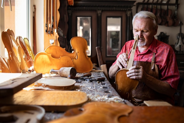 Senior carpenter assembling parts of violin instrument in his carpenter's workshop