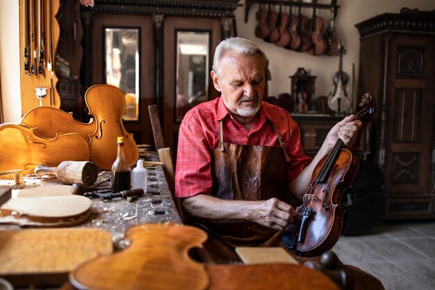 Senior carpenter craftsman polishing violin instrument in his carpenter's workshop