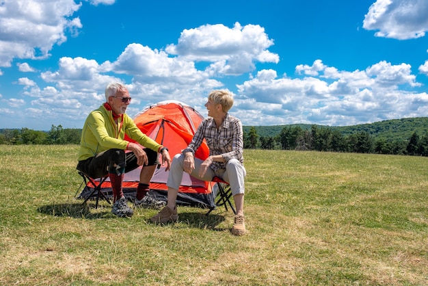 Senior couple having a rest in the field with a tent