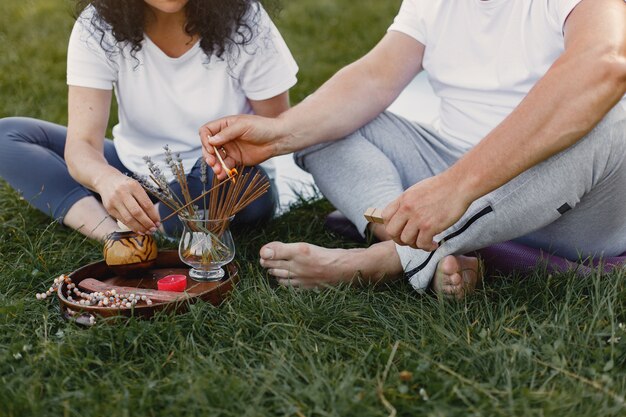 Senior couple is doing yoga outdoors. Stretching in park during sunrise. Brunette in a white t-shirt.