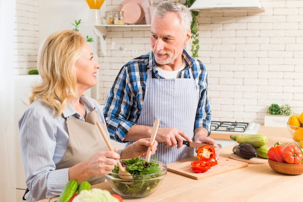 Senior couple preparing the salad in the modern kitchen looking at each other