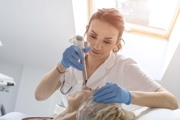 Senior female getting laser and ultrasound face treatment in a medical center