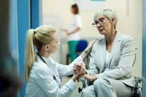 Free photo senior female patient in wheelchair feeling worried while communicating with female doctor and holding hands