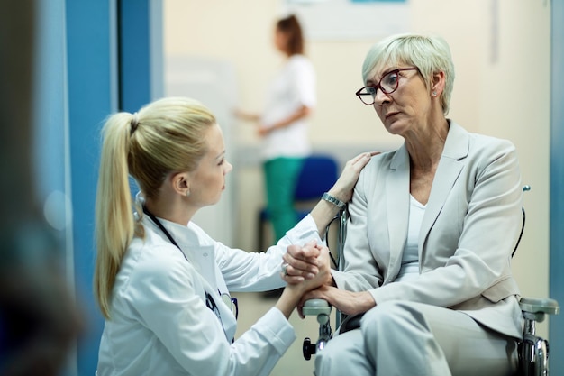 Free Photo senior female patient in wheelchair feeling worried while communicating with female doctor and holding hands