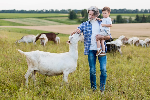 Senior holding little boy and play with goats