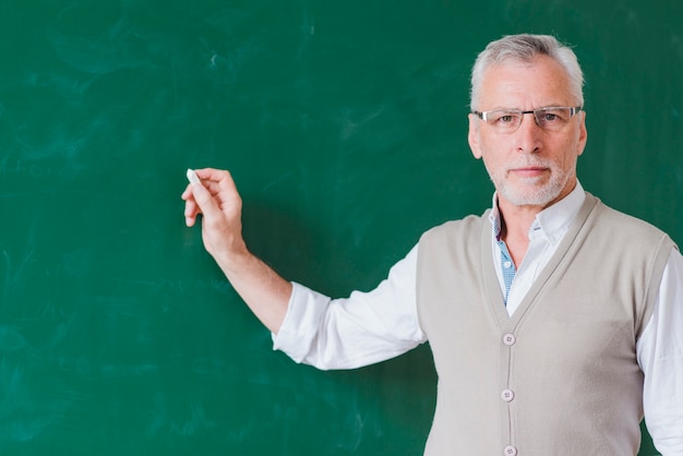 Free photo senior male teacher writing on green chalkboard