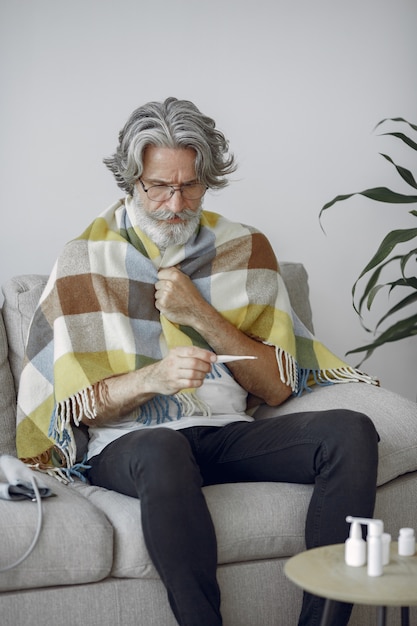 Free Photo senior man alone sitting on sofa. sick man covered with plaid. grangfather with thermometer.