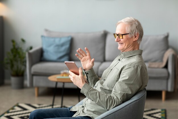 Senior man having a video call using tablet sitting on chair in living room