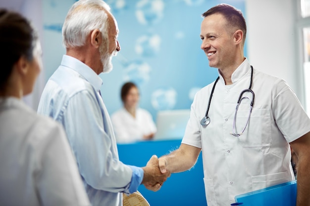 Free Photo senior man and his doctor shaking hands while greeting in a hallway at medical clinic focus is on doctor