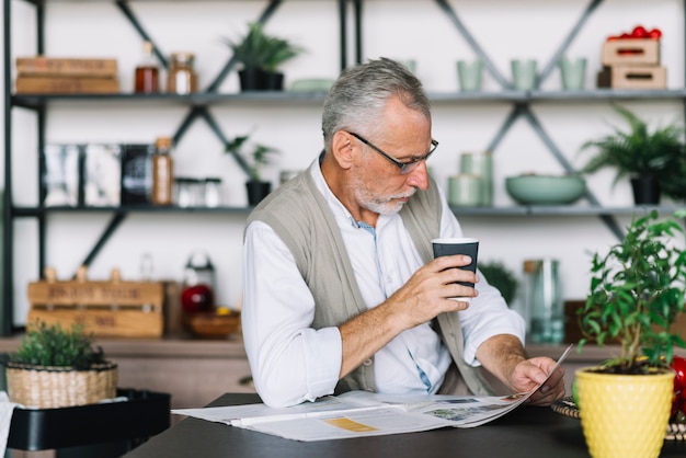 Free photo senior man holding coffee cup in hand reading newspaper