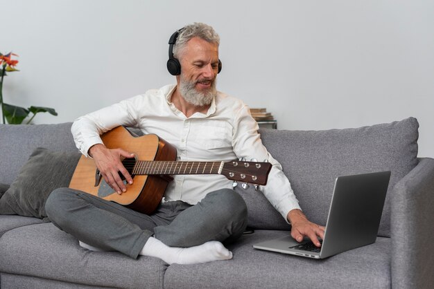 Senior man at home on the couch using laptop to study guitar lessons