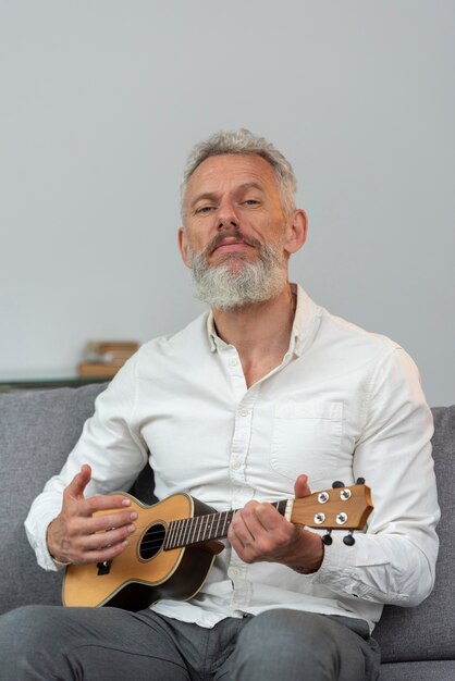 Senior man at home playing ukulele on the couch