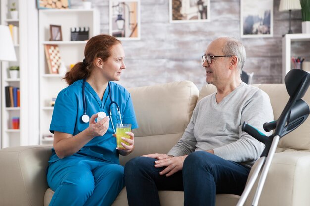 Senior man in nursing home smiling to the nurse while she's giving him pills.