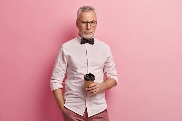 Senior man in pink shirt and black bowtie holding coffee cup