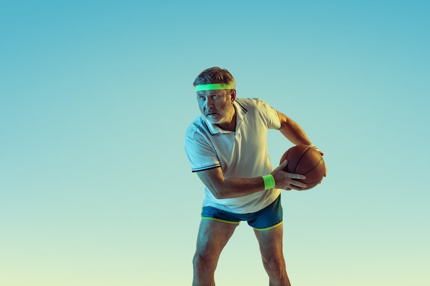 Senior man playing basketball on gradient wall in neon light