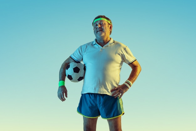 Senior man playing football in sportwear on gradient background and neon light