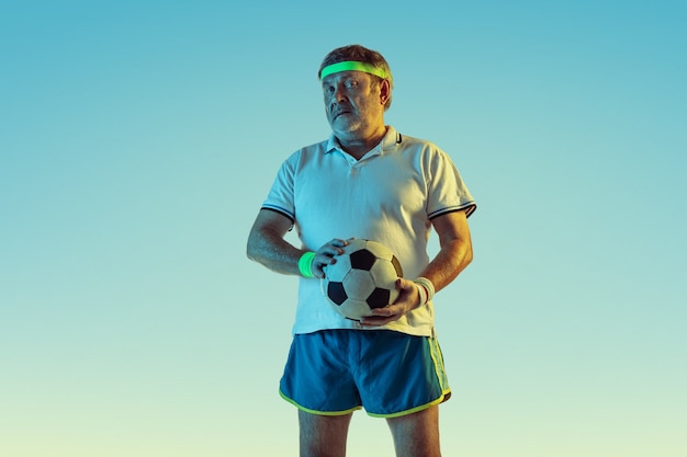 Senior man playing football in sportwear on gradient background and neon light