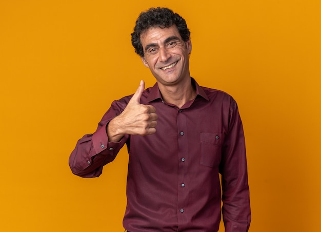 Senior man in purple shirt looking at camera smiling confident showing thumbs up 