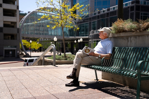 Free Photo senior man reading book on bench outdoors