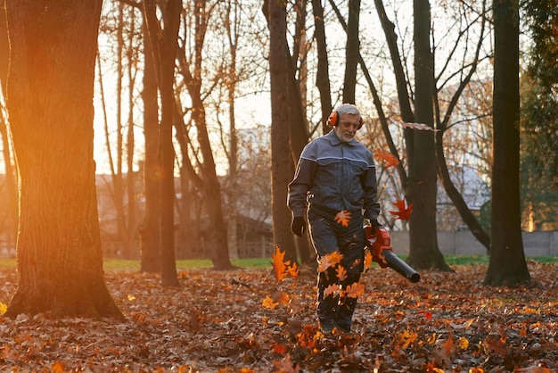 Free photo senior man removing trees leaves from backyard with portable blower front view of mature male