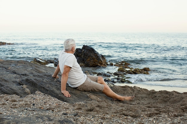 Free photo senior man resting at the beach and admiring the ocean