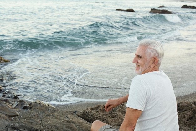 Free photo senior man resting at the beach and admiring the ocean