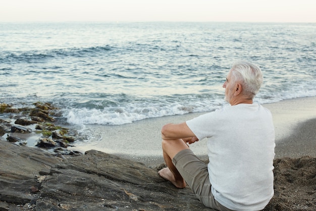 Free photo senior man resting at the beach and admiring the ocean