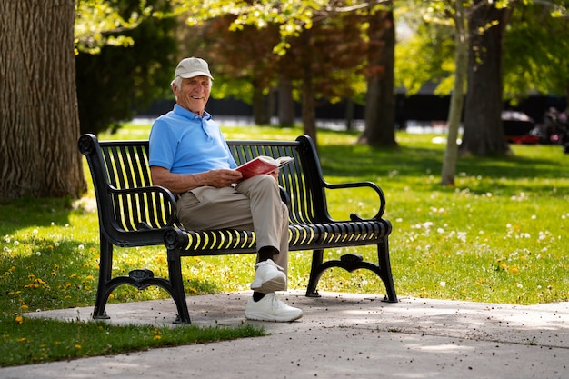 Senior man sitting on a bench outdoors and reading book