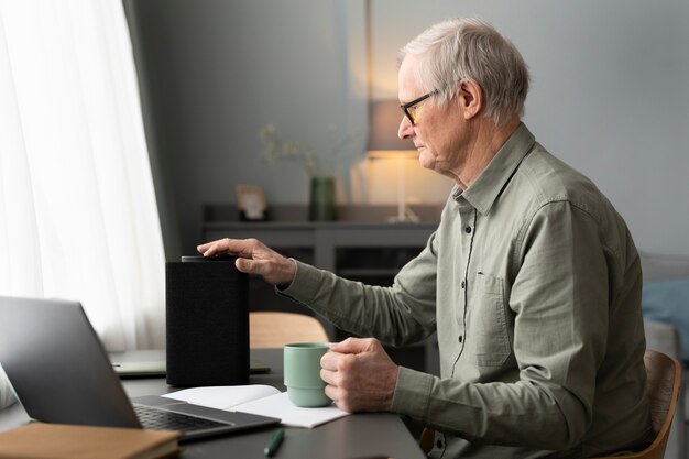 Senior man sitting at desk turning on a speaker in living room