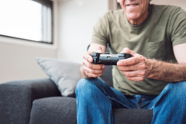 Senior man sitting on sofa playing video game at home