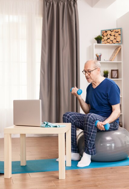 Senior man training biceps watching online fitness lesson