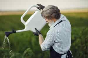 Free photo senior man watering his plants in his garden with sprinkle. man in a black apron.