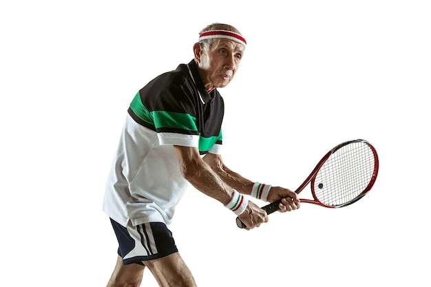 Free photo senior man wearing sportwear playing tennis isolated on white wall. caucasian male model in great shape stays active and sportive. concept of sport, activity, movement, wellbeing. copyspace, ad.