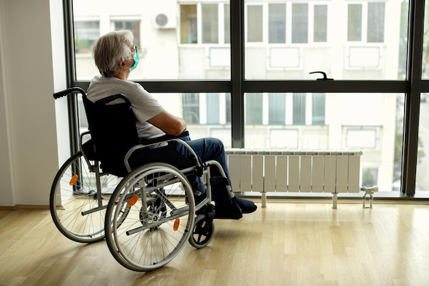 Free photo senior man in wheelchair looking through the window during covid19 lockdown