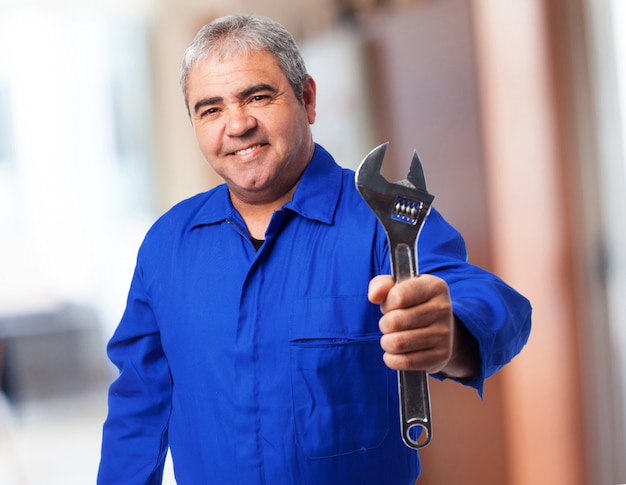 Senior man with blue jumpsuit holding a wrench