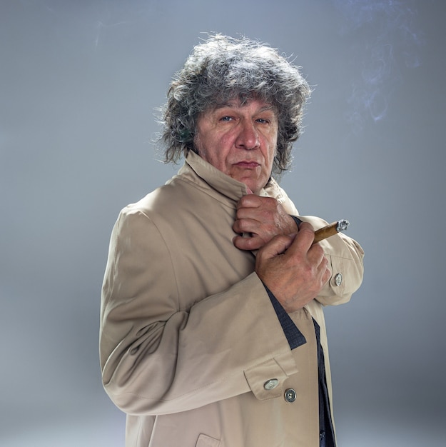 Free Photo the senior man with cigar as detective or boss of mafia on gray studio background