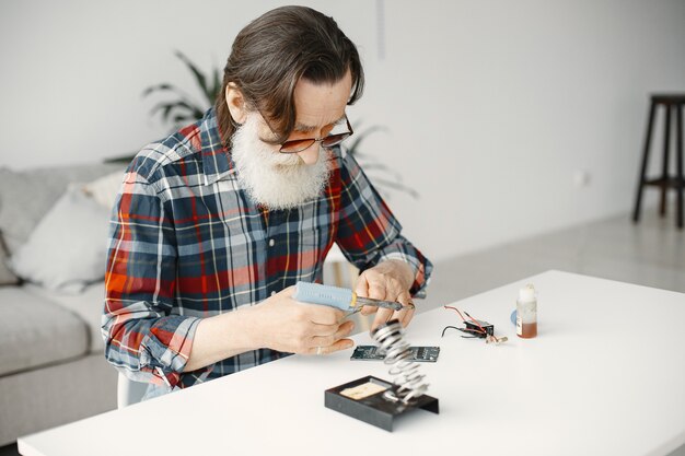 Senior man with equipment for soldering. Working at home.