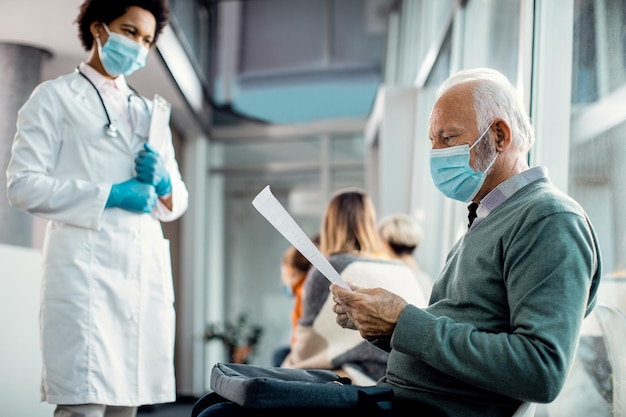 Free photo senior man with face mask reading his medical report at the hospital